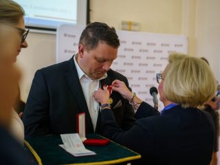 Kobieta przypina odznaczenie do marynarki mężczyzny podczas uroczystości.