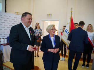 Odznaczony mężczyzna stoi obok kobiety z medalem na wstędze, trzymając czerwone etui.