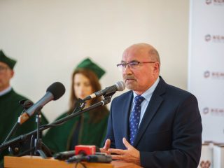 Mężczyzna w okularach i niebieskim krawacie przemawia do mikrofonów podczas inauguracji.