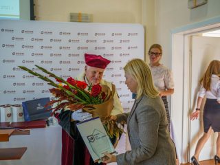 Rektor z bukietem kwiatów stoi obok kobiety trzymającej oprawiony dokument.