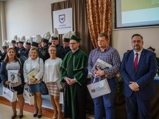 Grupa osób z dyplomami, książkami i torbami pozuje przed chórem górniczym.