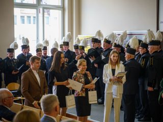 Uczestnicy z dyplomami i nagrodami stoją przed chórem w mundurach górniczych.