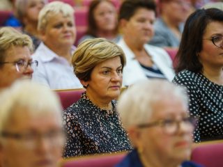 Uczestniczki uroczystości siedzą w rzędach czerwonych foteli.