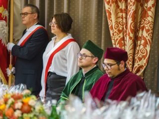 Poczet sztandarowy stoi obok przedstawicieli uczelni w zielonej i bordowej todze.