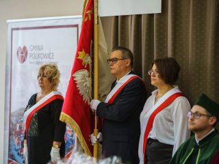 Troje członków pocztu sztandarowego stoi z biało-czerwonymi szarfami przy sztandarze.