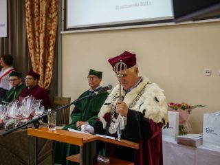Rektor trzyma berło i odczytuje przemówienie przy mównicy.