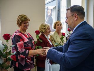 Kobieta we wzorzystej bluzce odbiera gratulacje od mężczyzny w niebieskim garniturze.