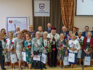 Uczestnicy inauguracji PUTW pozują z rektorem, trzymając czerwone róże, dyplomy i torby upominkowe.