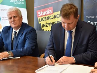 Mężczyzna w granatowym garniturze podpisuje umowę obok przedstawiciela UJW.