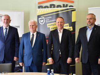 Czterej uczestnicy spotkania pozują przed banerami PeBeKa i UJW.