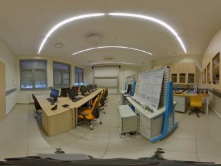 Panorama laboratorium z komputerami i tablicami urządzeń dydaktycznych.