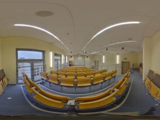 Sferyczna panorama sali wykładowej z rzędami foteli i pulpitów.