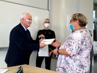 Kobieta w kwiecistej bluzce odbiera dyplom od mężczyzny w garniturze.