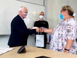 Siwowłosy mężczyzna i kobieta w kwiecistej bluzce dotykają się pięściami podczas wręczania nagród.