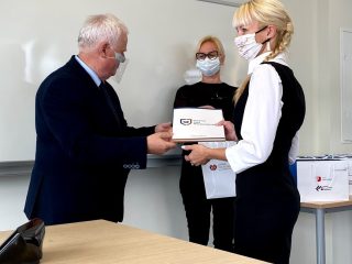 Kobieta w białej koszuli i czarnej kamizelce odbiera dyplom oraz książki.