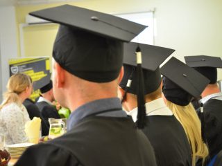 Absolwenci w biretach widoczni od tyłu podczas uroczystości wręczenia dyplomów.