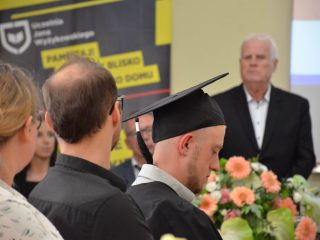 Widok zza siedzących gości na przemawiającego mężczyznę i bukiet kwiatów.