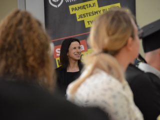 Uśmiechnięta kobieta siedzi przy stole prezydialnym na tle banera UJW.