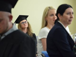 Uczestniczki uroczystości wręczenia dyplomów siedzą wśród absolwentów w biretach.