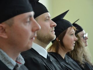 Czworo absolwentów w togach i biretach widocznych z boku podczas uroczystości.