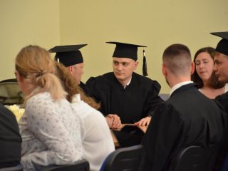 Absolwenci i goście rozmawiają, siedząc wokół stołu.