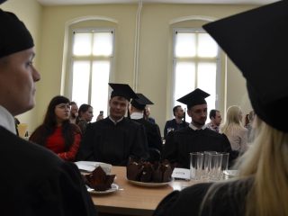 Uczestnicy uroczystości siedzą po obu stronach stołu, widoczni między biretami na pierwszym planie.