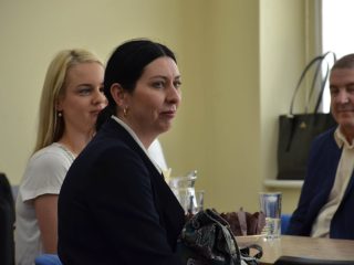 Kobieta w granatowej marynarce siedzi przy stole obok pozostałych gości uroczystości.