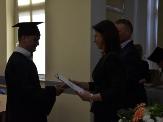 Absolwent w todze i birecie odbiera dokument od kobiety w czarnej marynarce.