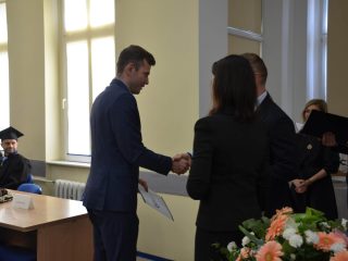 Mężczyzna w granatowym garniturze odbiera gratulacje podczas wręczania dyplomów.