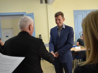 Uśmiechnięty mężczyzna w niebieskim garniturze ściska dłoń siwowłosego przedstawiciela uczelni.