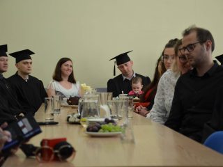 Absolwenci i ich goście siedzą wokół długiego stołu z napojami i poczęstunkiem.