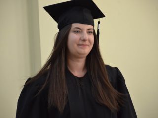 Portret absolwentki z długimi włosami w czarnej todze i birecie.