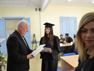 Absolwentka w todze trzyma dokument podczas rozmowy z przedstawicielem uczelni.