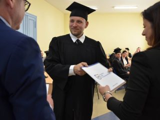 Absolwent w todze i birecie odbiera teczkę z logo UJW od organizatorki.