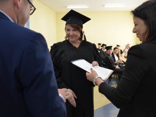 Uśmiechnięta absolwentka w birecie odbiera gratulacje i dyplom.