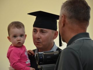 Absolwent w birecie trzyma małe dziecko podczas rozmowy przed kamerą.