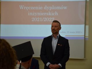 Prelegent w granatowej marynarce stoi przed ekranem z napisem Wręczenie dyplomów inżynierskich 2021/2022.