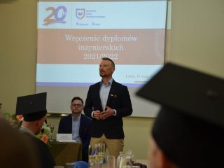 Mężczyzna gestykuluje podczas przemówienia przed absolwentami w biretach.