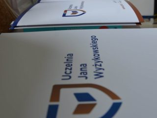 Rząd teczek z logo Uczelni Jana Wyżykowskiego przygotowanych do wręczenia.