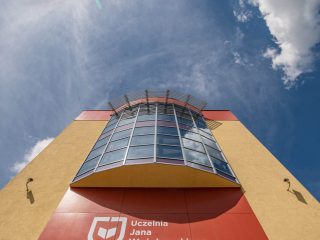Widok od dołu na przeszklony narożnik i logo UJW na czerwonej elewacji.