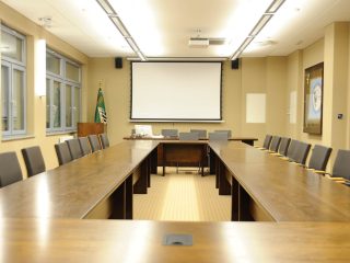 Sala konferencyjna UJW ze stołami ustawionymi w podkowę i ekranem.