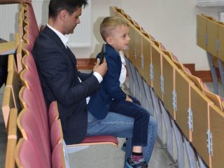 Mężczyzna i chłopiec siedzą obok siebie w rzędzie foteli w auli.