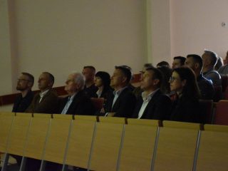 Publiczność ogląda prezentację w przyciemnionej auli.
