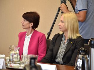 Dwie uczestniczki słuchają wystąpienia przy stole konferencyjnym.