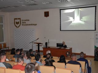 Projekcja filmu w auli podczas wykładu o ratownictwie, z publicznością widoczną od tyłu.