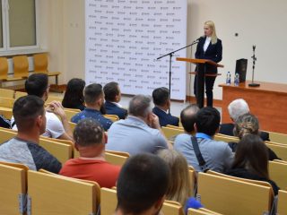 Publiczność słucha kobiety przemawiającej przy mównicy w auli UJW.