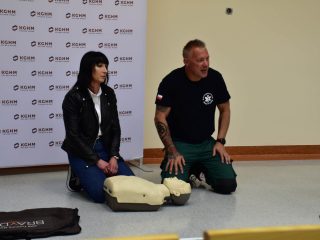 Ratownik i uczestniczka klęczą przy fantomie do nauki resuscytacji podczas pokazu pierwszej pomocy.