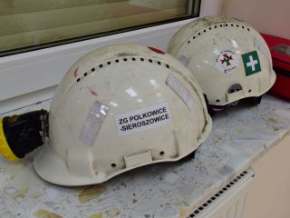 Dwa białe hełmy ratownicze na parapecie, jeden z oznaczeniem ZG Polkowice-Sieroszowice.