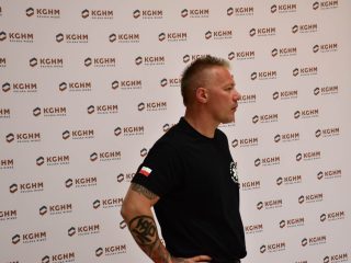 Ratownik w czarnej koszulce przemawia na tle logotypów KGHM.