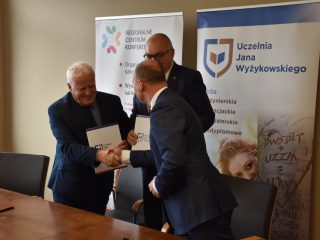 Przedstawiciel UJW podaje dłoń uczestnikowi spotkania, trzymając teczkę z dokumentami.